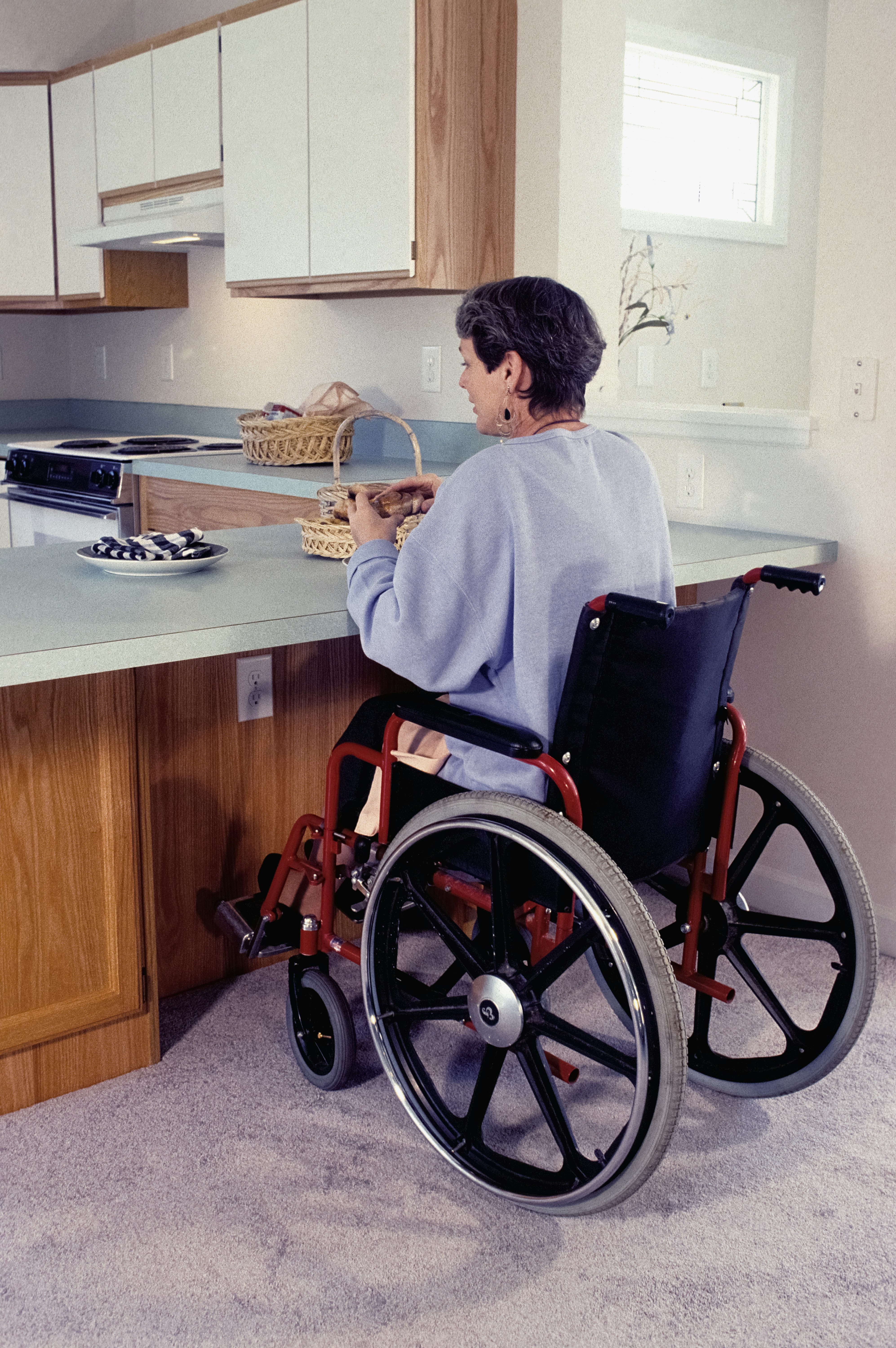 Wheelchair user reaching a kitchen drawer in an accessible home