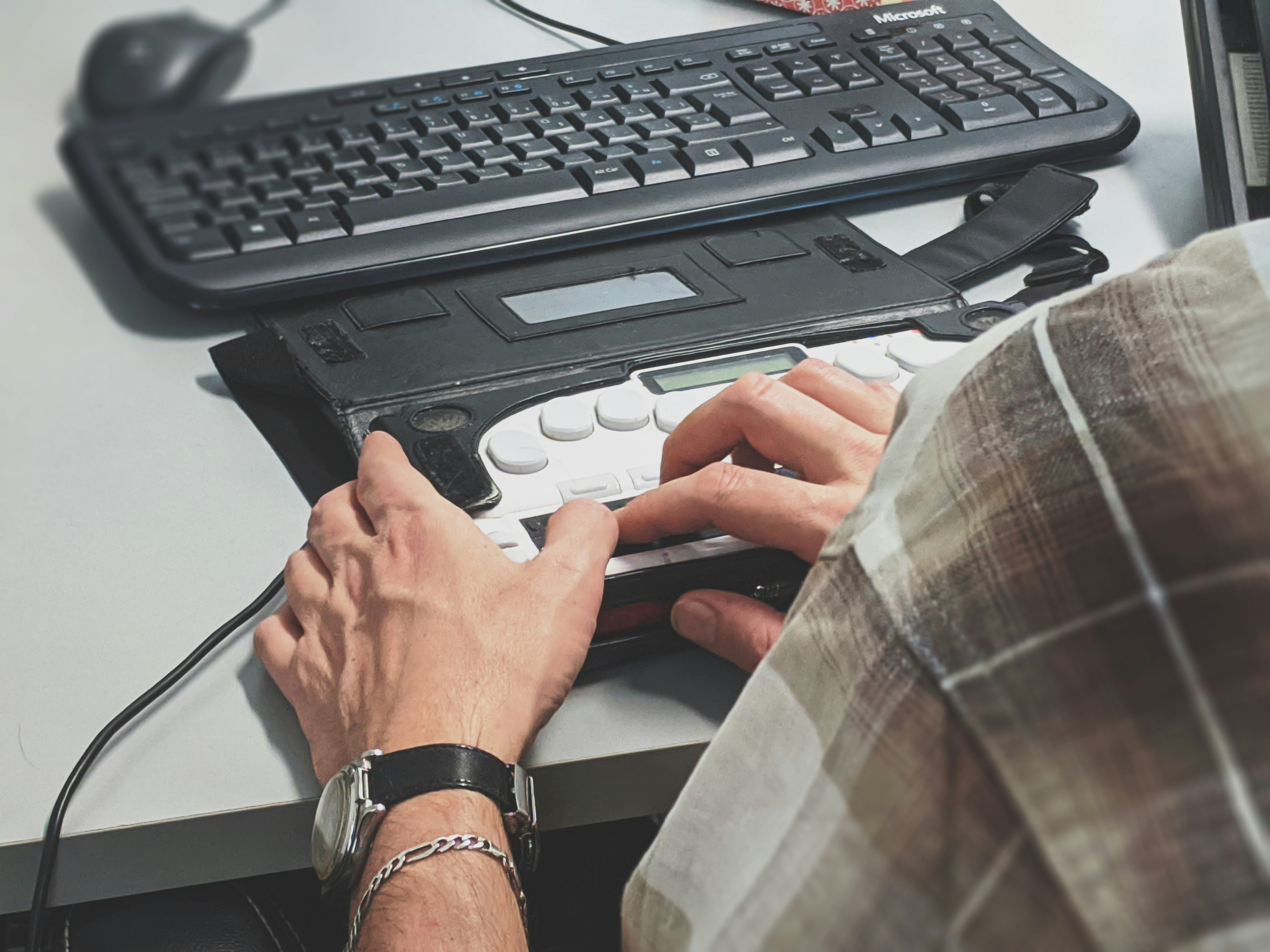 Hands using an assistive braille-style keyboard beside a computer