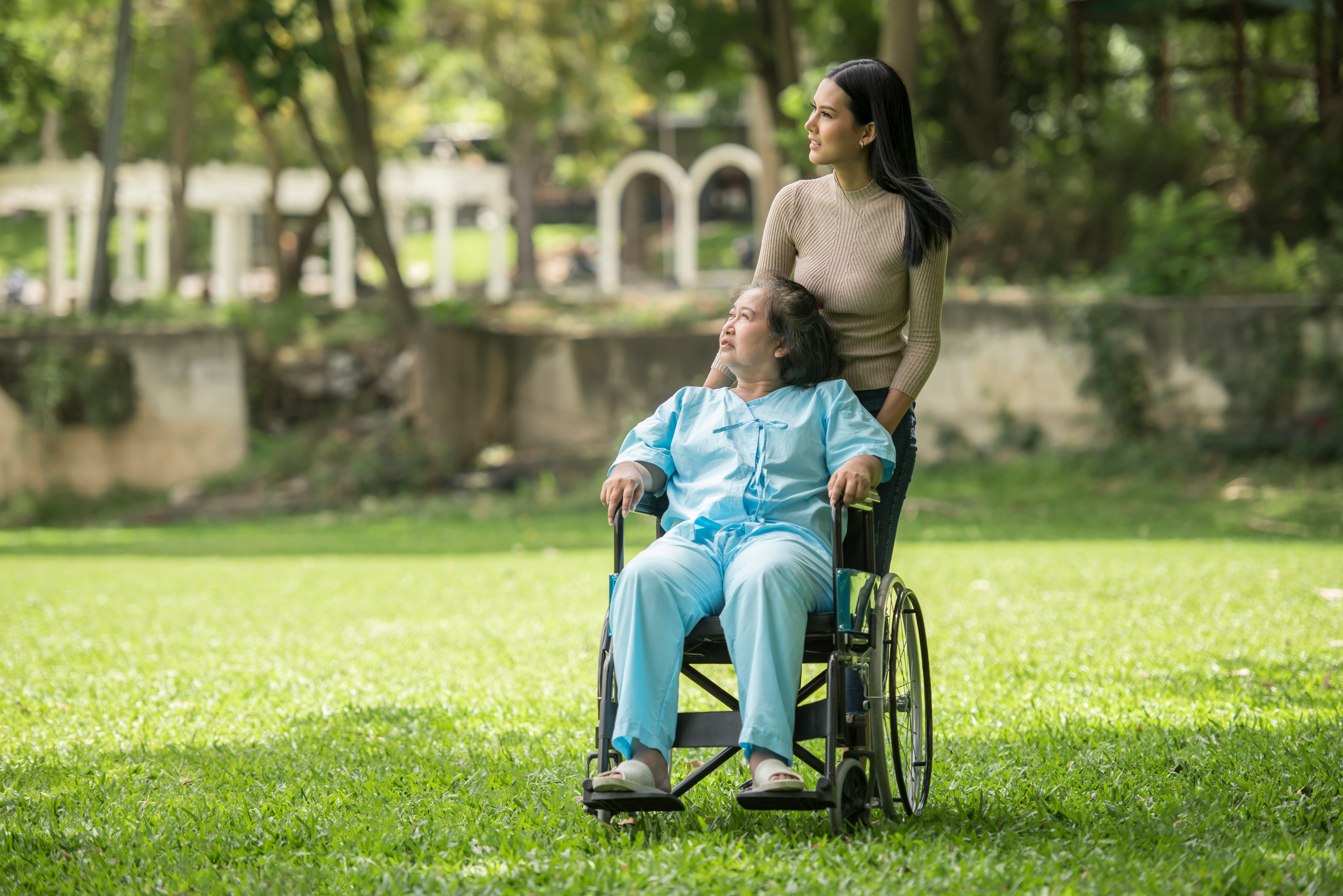 Caregiver pushing a wheelchair user through a park path