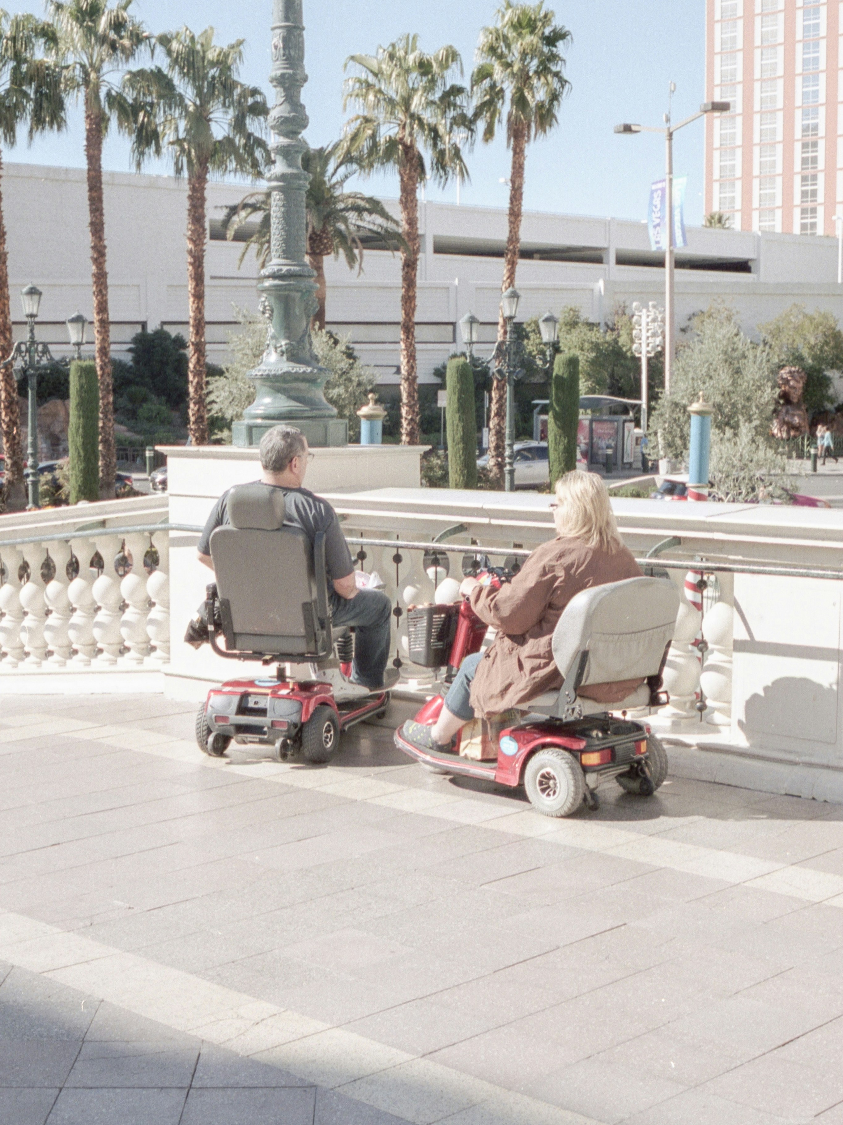 Two people using mobility scooters outdoors on a terrace